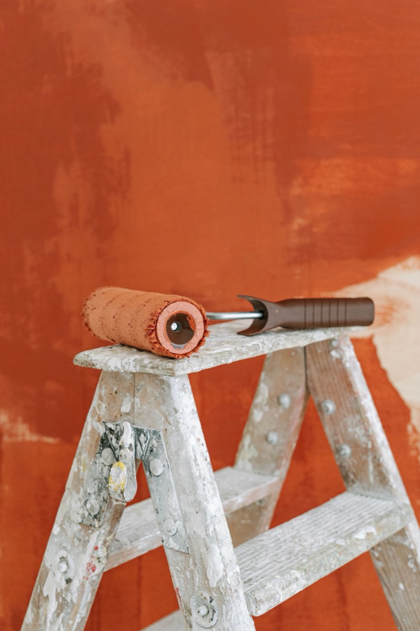 Malerin trägt Terrakotta-Farbe mit der Rolle auf eine Wand auf